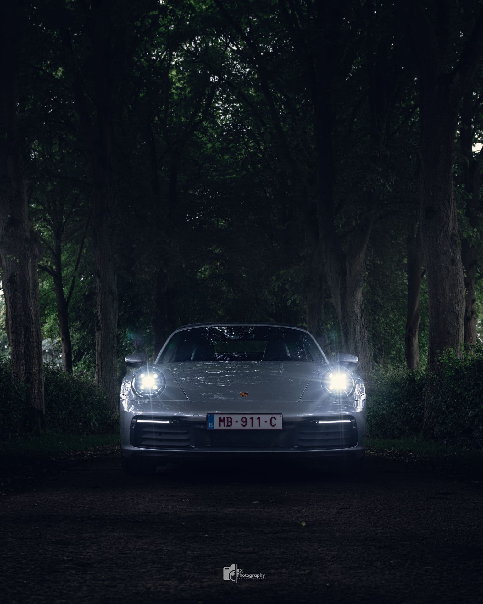 Porsche 911, phares allumés dans la pénombre d'une forêt belge